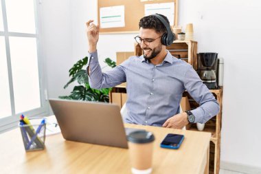 Genç Arap adam ofiste müzik dinlerken kendinden emin gülümsüyor.