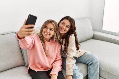 Genç çift mutlu bir şekilde gülümsüyor. Evdeki akıllı telefonun yanında selfie çekiyorlar..