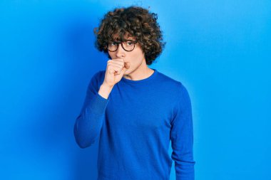Handsome young man wearing casual clothes and glasses feeling unwell and coughing as symptom for cold or bronchitis. health care concept. 