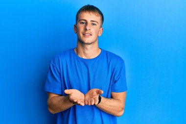 Young caucasian man wearing casual blue t shirt smiling with hands palms together receiving or giving gesture. hold and protection 