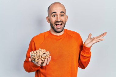 Fıstık tutan genç kel adam başarıyı mutlu bir gülümsemeyle ve kazanan yüz ifadesiyle kutluyor. 