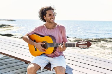Genç İspanyol adam klasik gitar çalıyor sahilde bankta oturuyor..