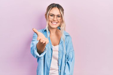 Güzel, genç, sarışın bir kadın. Günlük kıyafetler ve gözlük takıyor. Gülümsüyor, dostça tokalaşıyor. başarılı iş. 