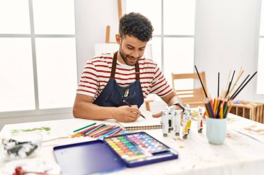 Sanat stüdyosunda gülümseyen genç Arap ressam mutlu çizimler yapıyor..