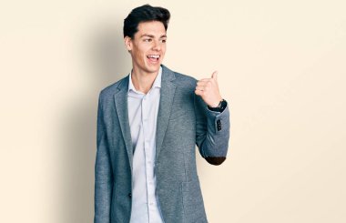 İş kıyafetleri giymiş, gülen, gülümseyen, gülümseyen ve baş parmağıyla yüzünü gösteren İspanyol bir genç.. 