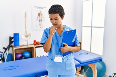 Kısa saçlı İspanyol bir kadın ağrı kesici kliniğinde çalışıyor kendini iyi hissetmiyor ve soğuk algınlığı veya bronşitin belirtisi olarak öksürüyor. sağlık hizmeti kavramı. 