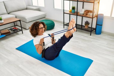 Olgun İspanyol kadın evdeki oturma odasında lastik bantlarla egzersiz yapıyor.