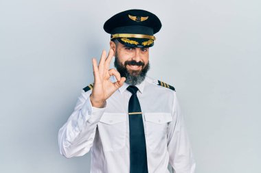 Uçak pilotu üniforması giyen genç İspanyol adam gülümsüyor ve el ve parmaklarıyla 