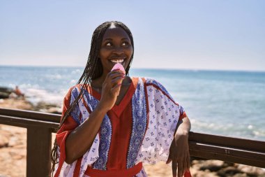 Genç Afrikalı Amerikalı kadın gülümseyerek sahilde dondurma yiyor..