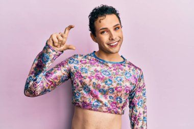 Handsome man wearing make up wearing fashion clothes smiling and confident gesturing with hand doing small size sign with fingers looking and the camera. measure concept. 