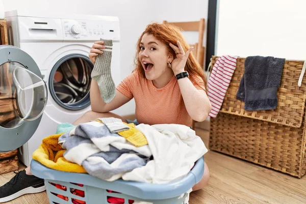 若い赤毛の女性は 噂やゴシップに耳を傾け手で笑みを浮かべて洗濯機に汚れた洗濯を入れて 聴覚障害の概念 — ストック写真