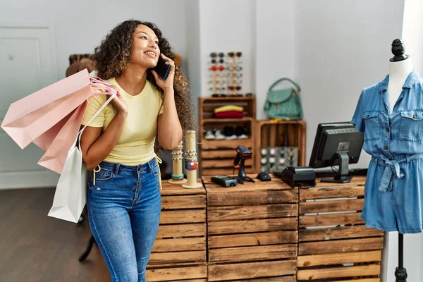 Alışveriş torbaları tutan ve giyim mağazasındaki akıllı telefondan konuşan genç Latin müşteri kadın..