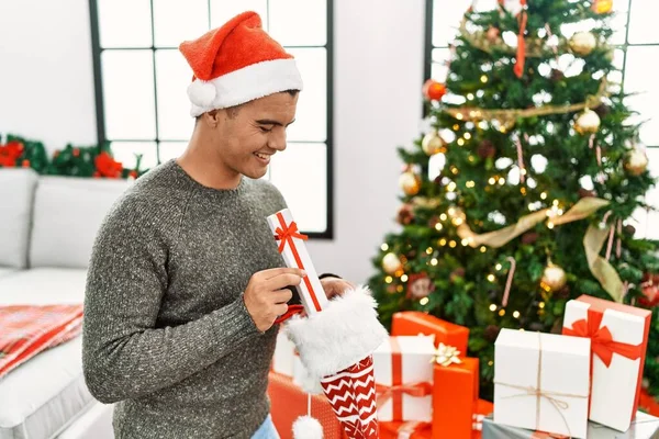 Young Hispanic Man Putting Gifts Christmas Sock Home — Foto de Stock