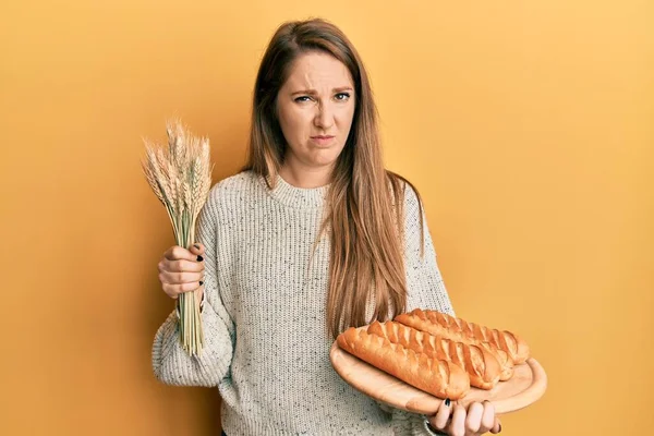 年轻的金发女人手里拿着自制的面包 带着对小麦的怀疑和紧张 因为问题皱着眉头 消极的人 — 图库照片