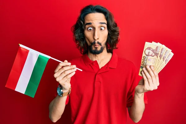 Joven Hombre Hispano Sosteniendo Bandera Húngara Forints Haciendo Cara Pez —  Fotos de Stock