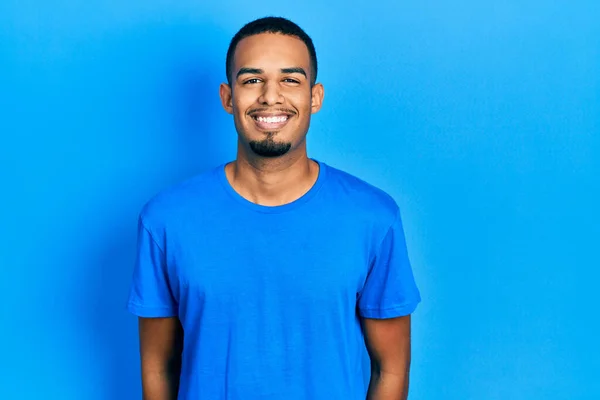 若いアフリカ系アメリカ人の男性が幸せとクールな笑顔でカジュアルなブルーのTシャツを着ています 運のいい人 — ストック写真