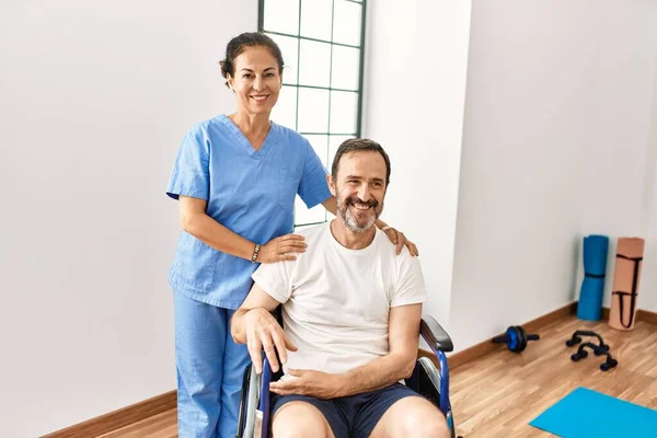リハビリテーションクリニックで車椅子と看護師に座っているヒスパニック系の中年男性ポジティブで幸せな立ち姿と笑顔で自信を持って笑顔を見せて歯 — ストック写真