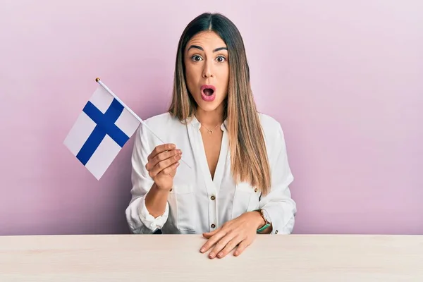 Mujer Hispana Joven Sosteniendo Bandera Finlandia Sentada Mesa Asustada Asombrada —  Fotos de Stock