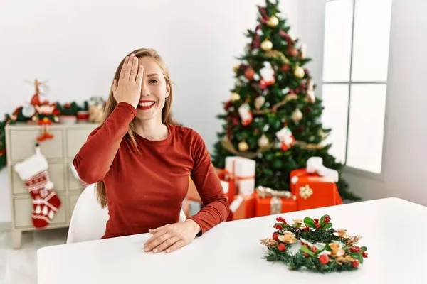 Kavkazská Mladá Blondýnka Sedící Stole Vánočního Stromku Zakrývajícího Jedno Oko — Stock fotografie