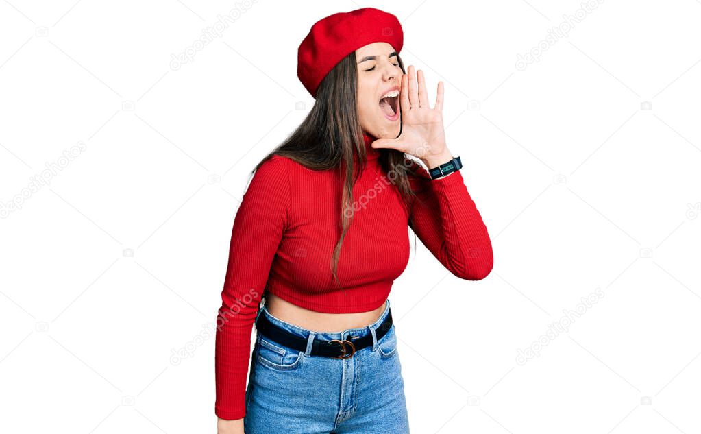 Young brunette teenager wearing french look with beret shouting and screaming loud to side with hand on mouth. communication concept. 