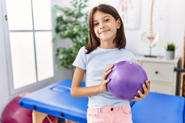 Genç İspanyol kız elinde küçük bir rehabilitasyon topu tutuyor. Pozitif ve mutlu görünüyor. Kendine güvenen bir gülümsemeyle dişlerini gösteriyor. 