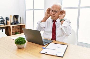 Ofiste çalışan üst düzey bir adam bilgisayar kullanıyor iki elini de kulak hareketlerini duymaya çalışıyor, dedikoduya meraklı. İşitme sorunu, sağır 