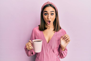 Genç esmer kız bir fincan kahve içiyor. Korkmuş ve ağzı açık kalmış, şaşırmış ve şaşırmış. İnanmayan yüz. 