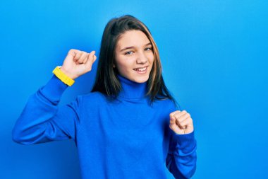 Balıkçı yaka kazak giyen genç esmer kız mutlu ve neşeli dans ediyor, gülümsüyor rahat ve kendinden emin bir şekilde müzik dinliyor. 