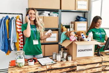 Yardım merkezinde çalışmaktan mutlu gülümseyen iki genç gönüllü kadın. Gülümseyen mutlu bir kız akıllı telefonda konuşuyor..