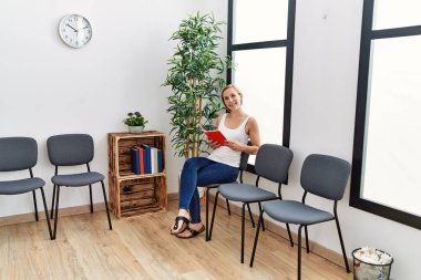 Bekleme odasında kendine güvenen beyaz bir kadın gülümsüyor.