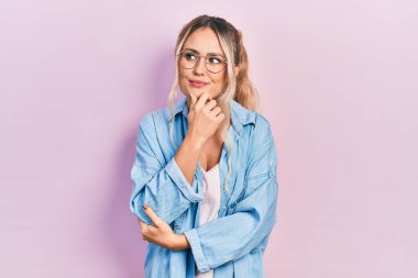 Güzel, genç, sarışın bir kadın. Günlük kıyafetler ve gözlük takıyor. Elleri çenesinde soru sormayı düşünüyor. Düşünceli bir yüzle gülümsüyor. şüphe kavramı. 