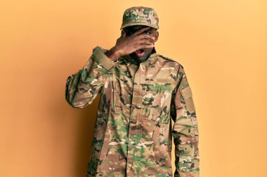 Genç Afro-Amerikan üniformalı asker şok içinde yüzünü ve gözlerini kapayarak utangaç ifadesiyle parmaklarının arasından bakıyor.. 