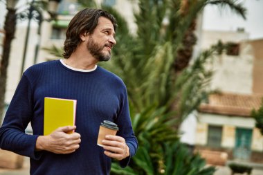 Orta yaşlı yakışıklı bir adam parkta bir fincan kahve içiyor.