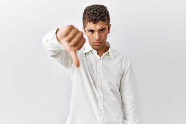 Young handsome hispanic man standing over isolated background looking unhappy and angry showing rejection and negative with thumbs down gesture. bad expression. 