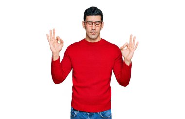 Yakışıklı İspanyol adam günlük kıyafetler ve gözlük takıyor rahatlıyor ve gözleri kapalı gülümsüyor parmaklarıyla meditasyon hareketi yapıyor. yoga konsepti. 