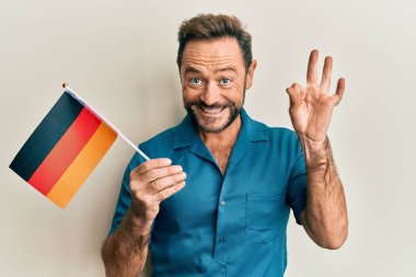 Orta yaşlı bir adam elinde Alman bayrağı tutuyor. Parmaklarıyla imza atıyor, gülümsüyor. Mükemmel bir sembol. 