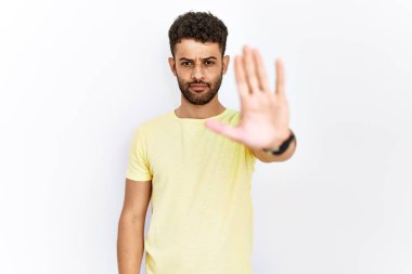 Arab young man standing over isolated background doing stop sing with palm of the hand. warning expression with negative and serious gesture on the face. 