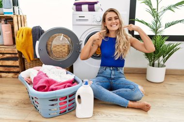 Çamaşır sepetinin yanında oturmuş gülümseyen ve parmaklarıyla ve ağzıyla işaret eden güzel bir kadın. diş sağlığı kavramı. 