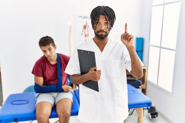 Kırık kollu bir adamla birlikte acı giderme kliniğinde çalışan genç İspanyol bir adam üzgün ve üzgün görünüyor, parmaklarıyla yön gösteriyor, mutsuz ve depresif.. 