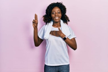 Young african american woman wearing sportswear and towel smiling swearing with hand on chest and fingers up, making a loyalty promise oath 