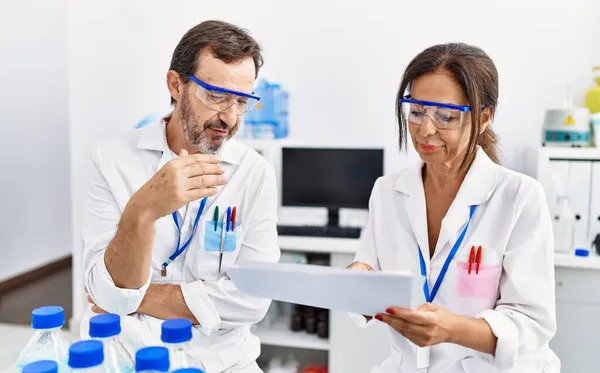 Medelålders Man Och Kvinna Partner Bär Vetenskapsman Uniform Läsning Dokument — Stockfoto