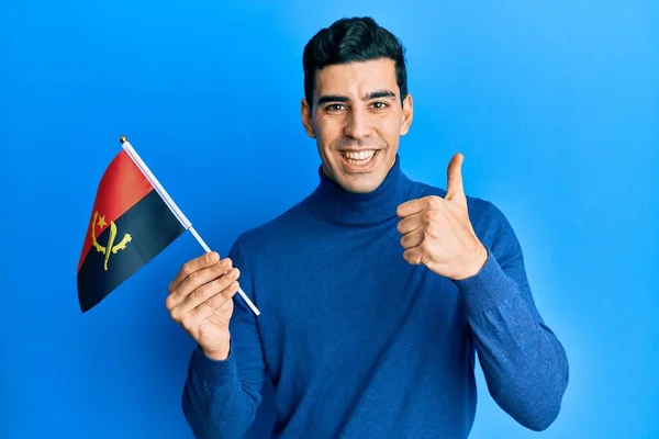 Hezký Hispánec Drží Angolskou Vlajku Usmívá Šťastně Pozitivně Palec Nahoru — Stock fotografie