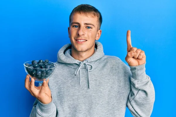 Young Caucasian Man Holding Bowl Blueberries Smiling Idea Question Pointing — стоковое фото