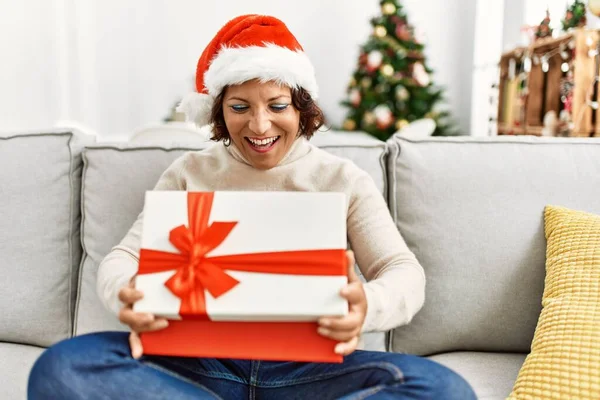 Middle Age Hispanic Woman Unboxing Gift Sitting Sofa Christmas Tree — Stock Photo, Image