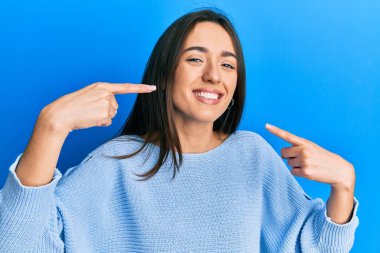 Günlük kıyafetler giyen, neşeli gülümseyen, parmaklarıyla ve ağzıyla işaret eden genç İspanyol kız. diş sağlığı kavramı. 