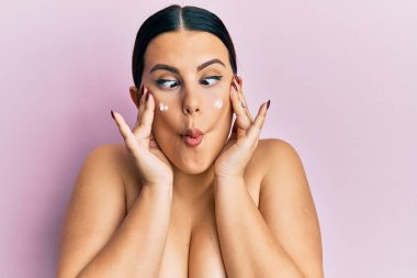 Güzel esmer kadın, üstsüz, yüz kremi sürmüş, balık suratlı, şaşı gözlü, çılgın ve komik.. 