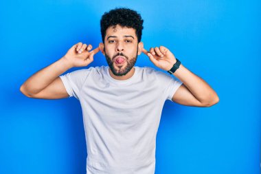 Young arab man with beard wearing casual white t shirt smiling pulling ears with fingers, funny gesture. audition problem 