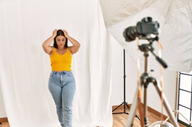 Young beautiful hispanic woman posing as model at photography studio suffering from headache desperate and stressed because pain and migraine. hands on head. 