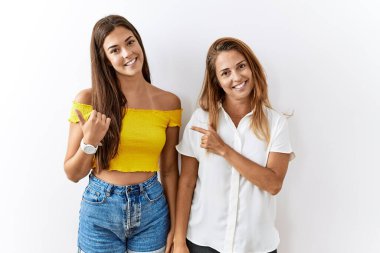 Mother and daughter together standing together over isolated background cheerful with a smile on face pointing with hand and finger up to the side with happy and natural expression 