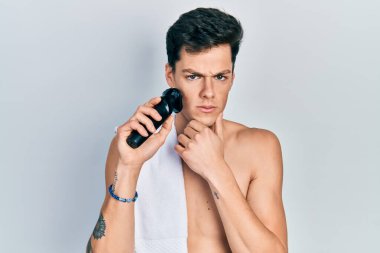 Elektrikli tıraş makinesiyle tıraş olan genç İspanyol adam şüpheci ve gergin, sorun yüzünden surat asıyor. negatif kişi. 